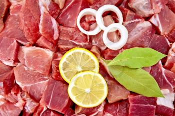 Texture of pieces of raw meat with bay leaf, rings of white onion and lemon slices