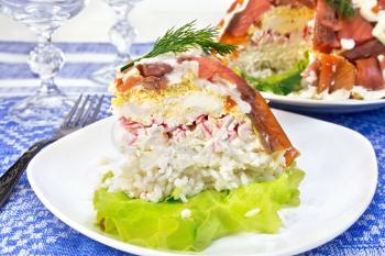 A piece of puff salad with salmon, egg, crab meat and rice, mayonnaise in a plate on a green salad on the background of the tablecloth