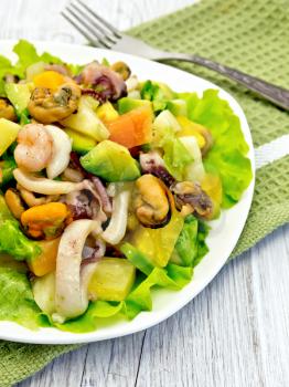 Salad with shrimp, octopus, mussels and calamari with avocado, lettuce and pineapple in a plate on a napkin on a light wooden board