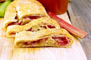 Strudel with rhubarb, stalks and mug on the background of wooden boards