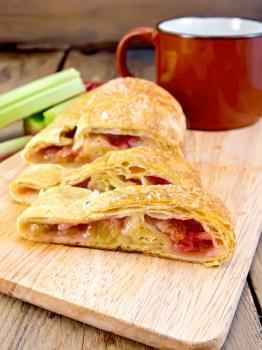 Strudel with rhubarb and a mug, stems on a wooden boards background