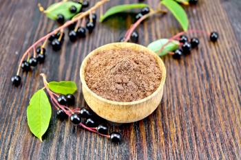Flour of bird-cherry in a bowl with berries on a background of wooden boards