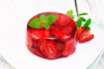 Strawberry jelly with mint and berries in a plate on a napkin on the background light wooden boards