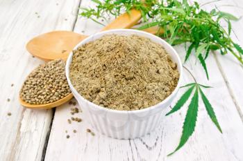 Hemp flour in bowl, grain in spoon, cannabis leaves on the background of the wooden boards