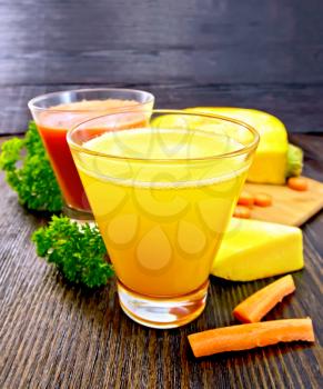 Two glassfuls juice of pumpkin and carrot, vegetables and parsley on a wooden board background