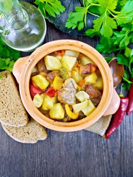 Roast with chicken, potatoes, squash and sweet peppers in a clay pot on a napkin of burlap, bread and parsley on a dark wooden board on top