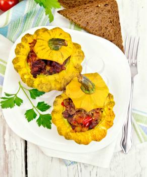 Two yellow squash stuffed with meat, tomatoes and peppers in the dish, bread, garlic, parsley and a napkin on a background of wooden boards on top