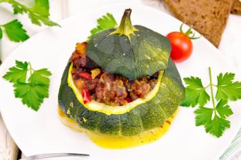 Squash green stuffed with meat, tomatoes and peppers in the dish, garlic and parsley on the background light wooden boards