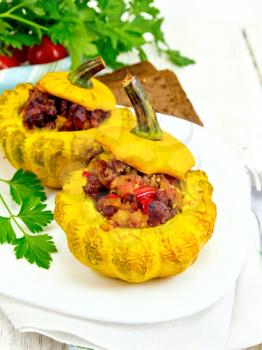 Two yellow squash stuffed with meat, tomatoes and peppers in the dish, bread, parsley and a napkin on a wooden boards background
