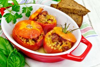 Tomatoes stuffed with meat and steamed wheat bulgur in a roasting pan on a napkin, bread, parsley and basil on a wooden boards background
