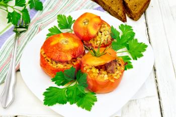 Tomatoes stuffed with meat and steamed wheat bulgur in a white plate, napkin, fork, bread and parsley on a wooden board background