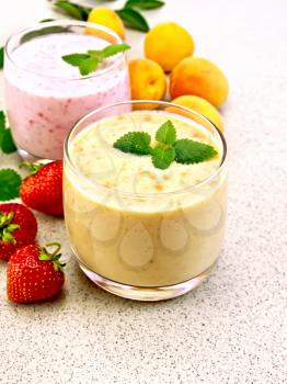 Two glasses of milk cocktail with apricots, strawberries and mint on the background of a granite table