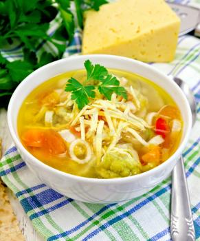 Minestrone soup with meat, celery, tomatoes, zucchini and cabbage, green peas, carrots and pasta, sprinkled grated cheese in a bowl on a towel, bread on the background light wooden boards