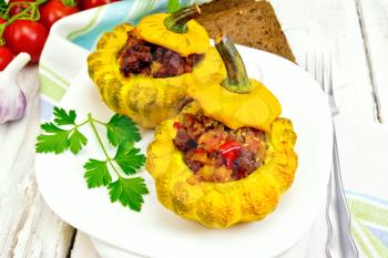 Two yellow squash stuffed with meat, tomatoes and peppers in the dish, bread, garlic, parsley and fork on a wooden board