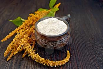 Flour amaranth in a clay cup, brown flower with green leaves on a background of wooden boards