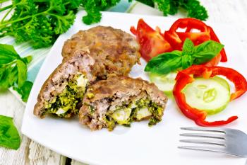 Cutlets stuffed with spinach and egg, salad with tomatoes, cucumber and pepper in a dish on a towel, basil and parsley on a wooden board background