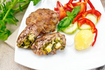 Cutlets stuffed with spinach and egg, slices of tomato, cucumber and pepper, cooked potatoes in a dish on a background of a granite table