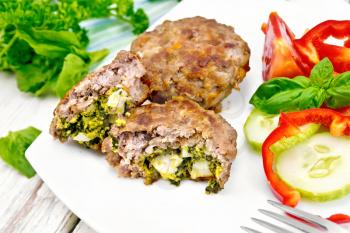 Cutlets stuffed with spinach and egg, salad with tomatoes, cucumber and pepper in a dish on a towel, basil and parsley on the background light wooden boards
