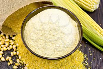 Flour corn in a bowl on the grits, cobs and grains, a bag on a dark wooden boards background