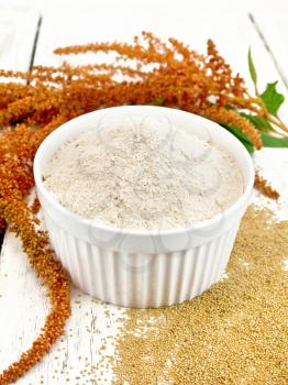 Amaranth flour in white bowl, seeds scattered on the table, brown flower with leaves on the background of wooden boards