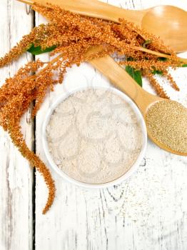 Flour amaranth in a bowl, a spoon with grain, brown flower with green leaves on the background of the wooden planks on top