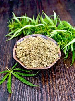 Hemp flour in a bowl, green cannabis leaves on the background of wooden boards