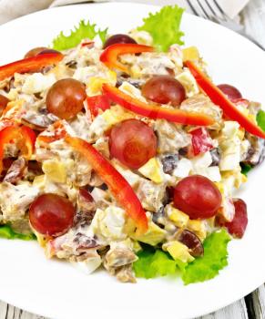 Salad of meat, salty soft feta cheese, sweet pepper, egg and grape with mayonnaise on lettuce in plate against the background of wooden boards