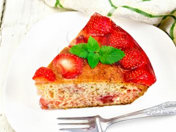 Piece of sweet pie with strawberries, kissel, jelly and mint, fork in white plate, a napkin on the background light wooden boards