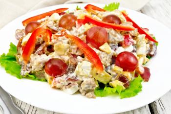 Salad of meat, salty soft feta cheese, sweet pepper, egg and grape with mayonnaise on lettuce the plate, fork on the background of wooden boards