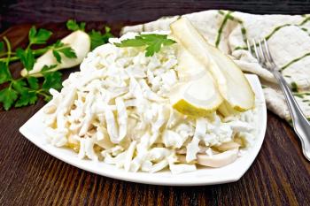 Salad of squid, rice, pears and eggs in a plate, parsley, a towel and a fork on the background of wooden boards