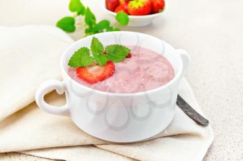 Strawberry soup with berries and mint in a bowl on a towel, spoon on a background of stone table