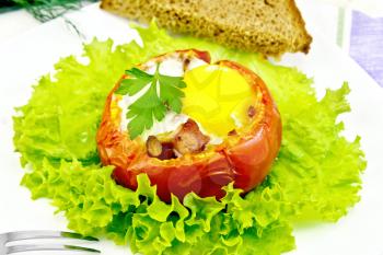 Scrambled eggs with ham and mushrooms in a tomato on a green lettuce in the plate, bread, fork and a napkin on a wooden boards background