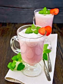 Strawberry soup in two glass goblets with berries and mint and spoon on a napkin against the background of wooden boards