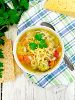 Minestrone soup with meat, celery, tomatoes, zucchini and cabbage, green peas, carrots and pasta, sprinkled grated cheese in a bowl on a napkin, bread on the background of wooden boards on top