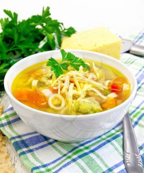 Minestrone soup with meat, celery, tomatoes, zucchini and cabbage, green peas, carrots and pasta, sprinkled grated cheese in a bowl on a napkin, bread on a wooden boards background