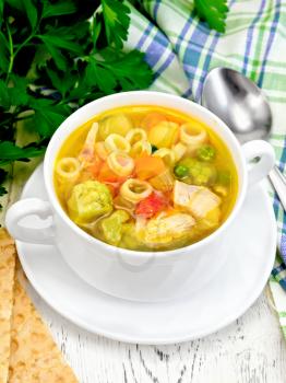 Minestrone soup with meat, celery, tomatoes, zucchini and cabbage, green peas, carrots and pasta in a bowl, towel, bread on a wooden boards background