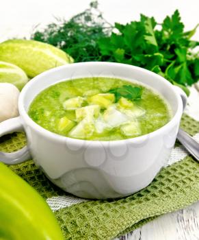 Cucumber soup with green peppers and garlic in a bowl on a napkin, parsley on the background light wooden boards