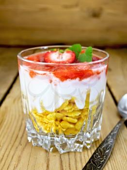 Milk dessert with strawberries, corn flakes and yogurt in a glass, a spoon on a background of wooden boards