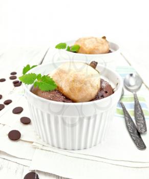 Two white bowl dessert with chocolate and pear, spoon, mint on a kitchen towel on the background of wooden boards