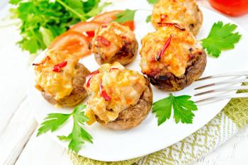 Mushrooms stuffed with meat and peppers with parsley and tomatoes in white plate on the towel, fork on the background light wooden boards
