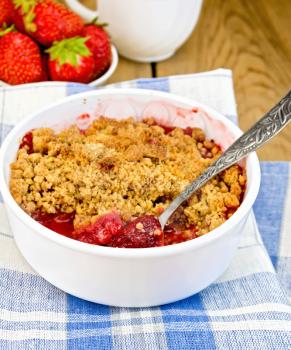 Strawberry crumble in a white bowl with a spoon on blue napkin on a wooden boards background