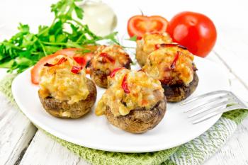 Mushrooms stuffed with meat and peppers with parsley and tomatoes in white plate on the towel, fork on the background of wooden boards