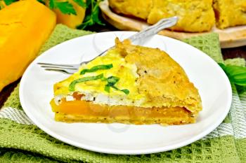 One piece of the pie of pumpkin, salty feta cheese, eggs, cream and herbs in a plate on towel, basil on a dark wooden board