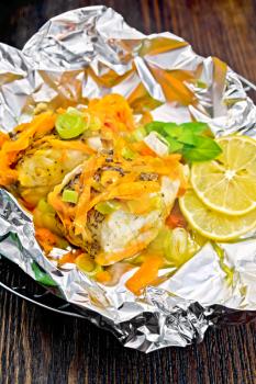Pike with carrots, leek, basil and slices of lemon in foil on the lattice on a wooden boards background