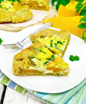 Two piece of the pie of pumpkin, salty feta cheese, eggs, cream and herbs in a plate on a napkin, parsley on the background light wooden boards