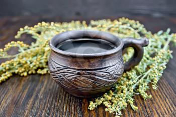 Herbal tea in a clay cup, twigs gray sagebrush, wormwood dried on a paper on the background of wooden boards