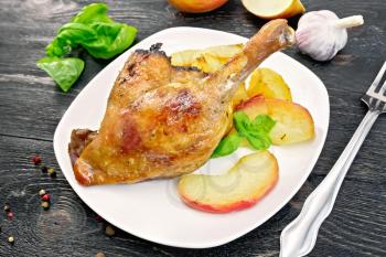 Roasted duck leg with apple, potatoes in a dish, basil, garlic and fork on the background of wooden boards