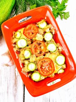 Casserole from minced meat, tomatoes and zucchini in a brazier against a light wooden board on top