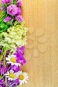 Frame of flowers of clover, chamomile, fireweed and meadowsweet on the background of a wooden board