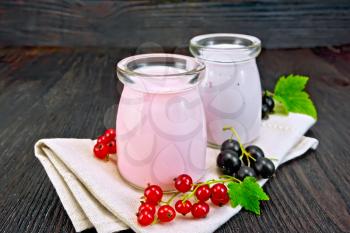 Milk cocktail with red and black currant in glass jars on a napkin with berries on a wooden board background